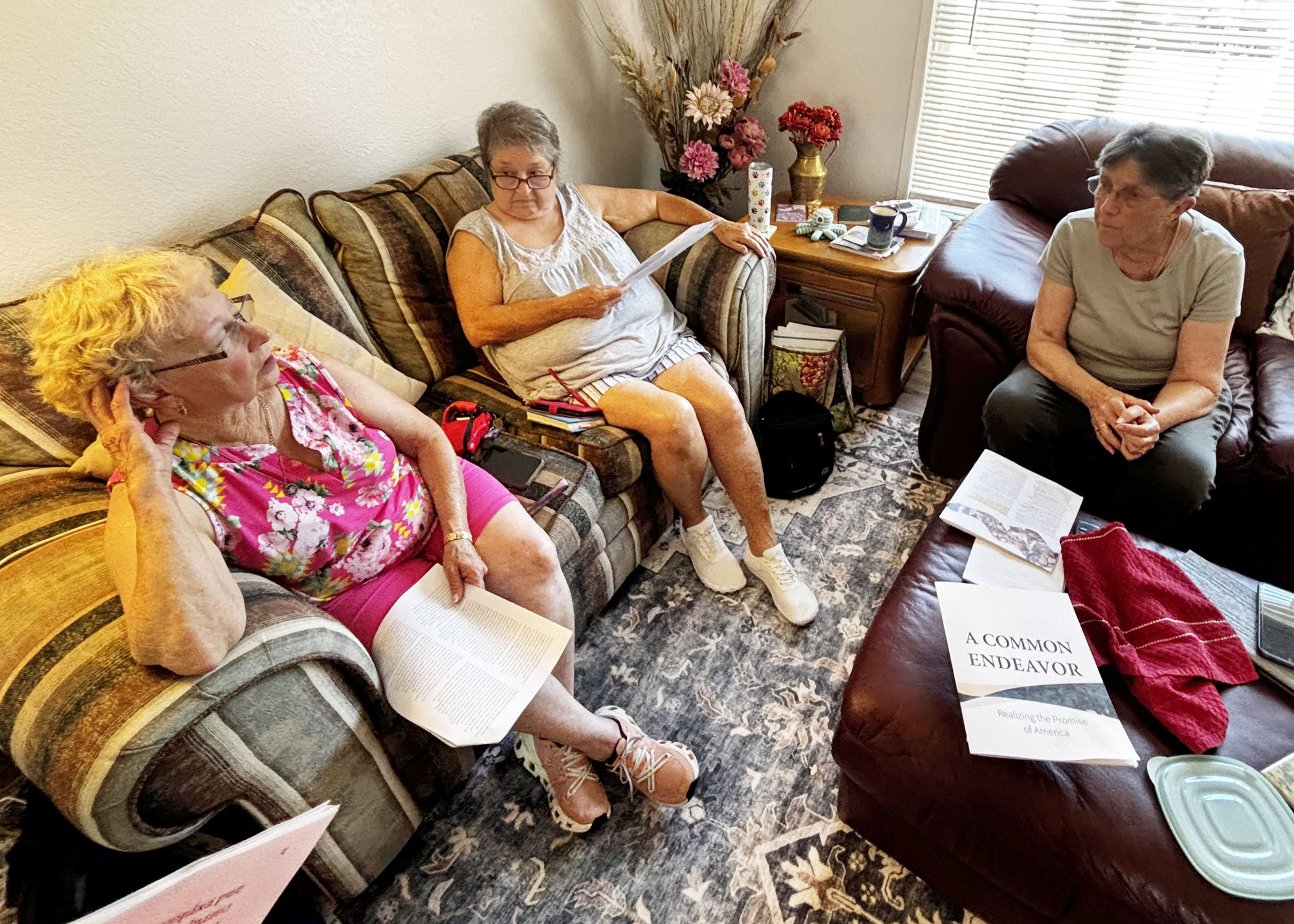 Three friends sit in a living room with the A Common Endeavor letter in their hands.